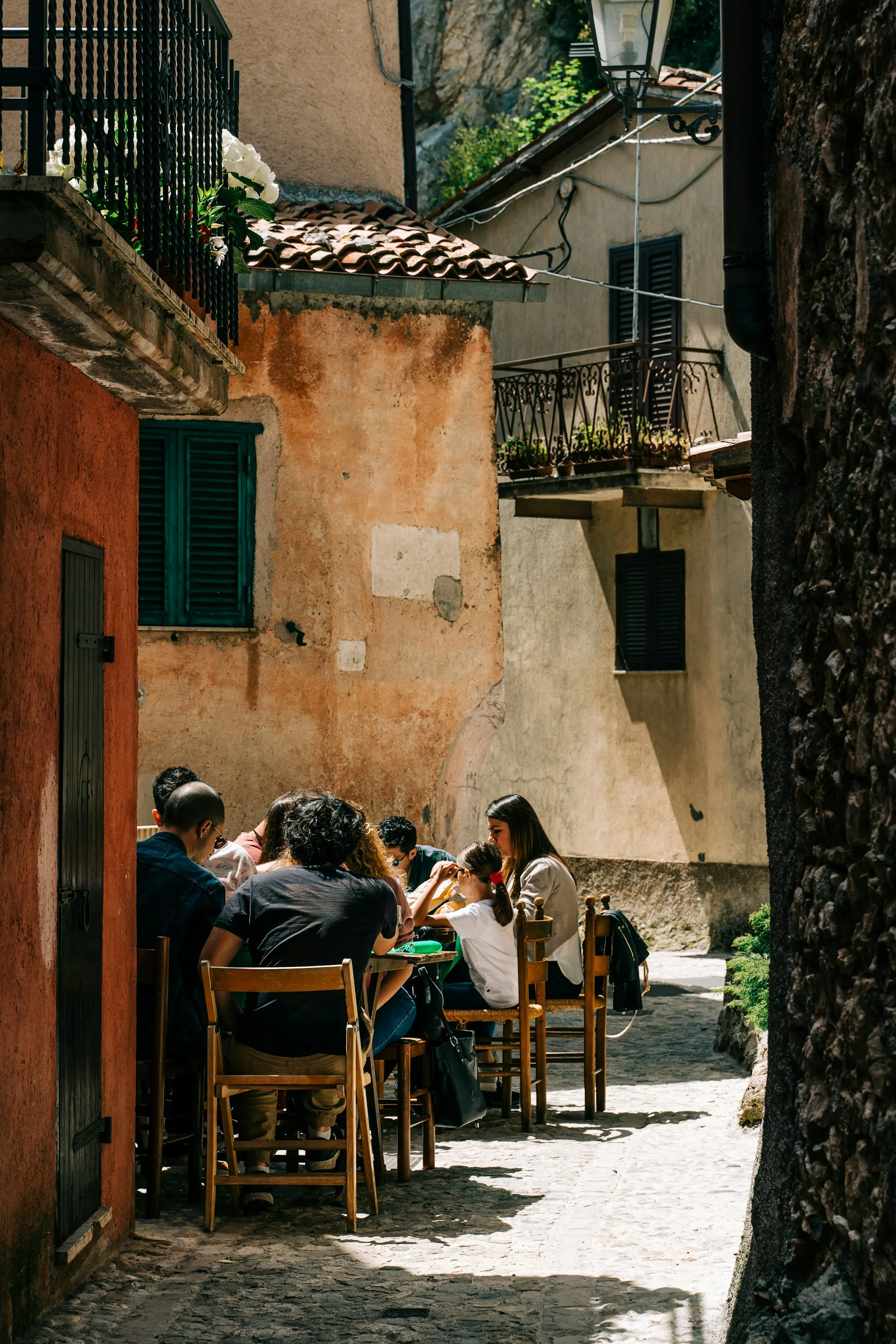 Friends sharing a long lunch at a table in a sunlit Mediterranean lane