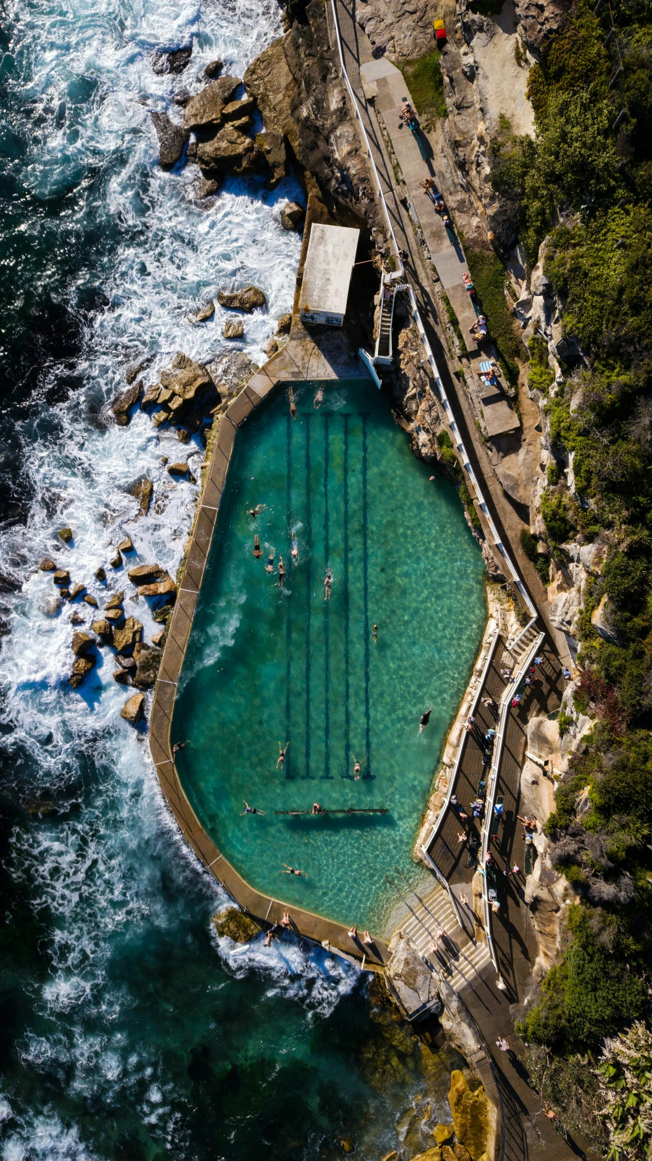 Swimmers in a rock-edged ocean pool beside the surf, seen from above