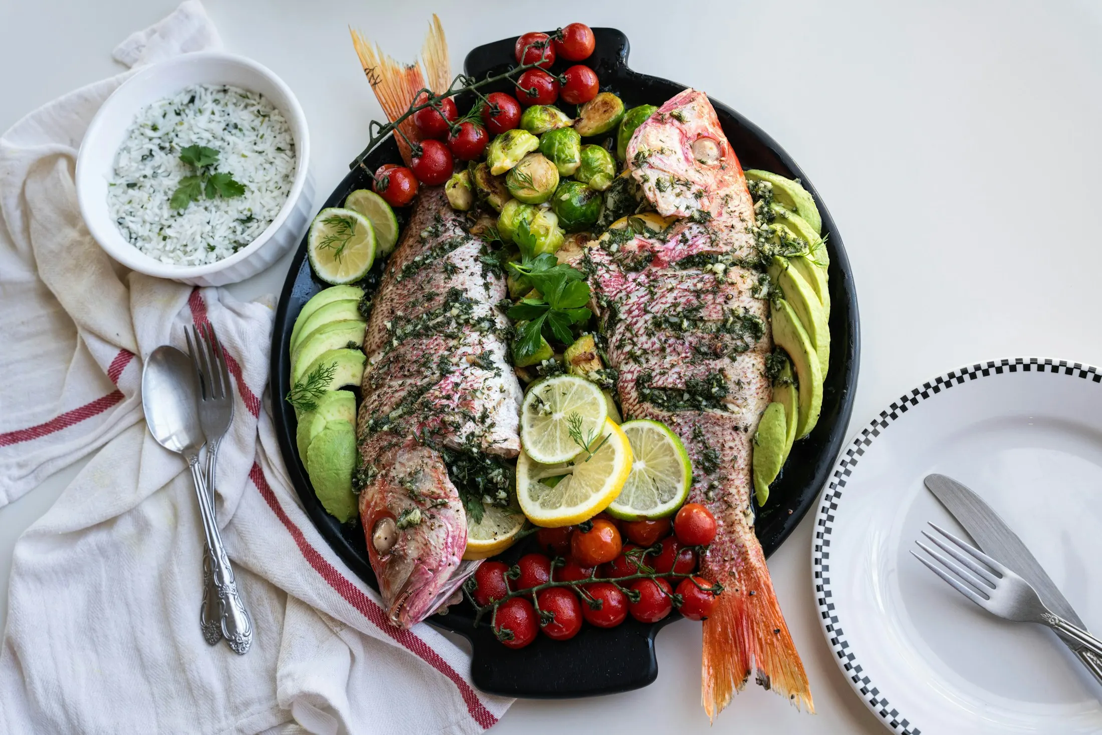 A platter of whole grilled red mullet with cherry tomatoes, avocado, cucumber and lemon, beside a yoghurt and herb dip
